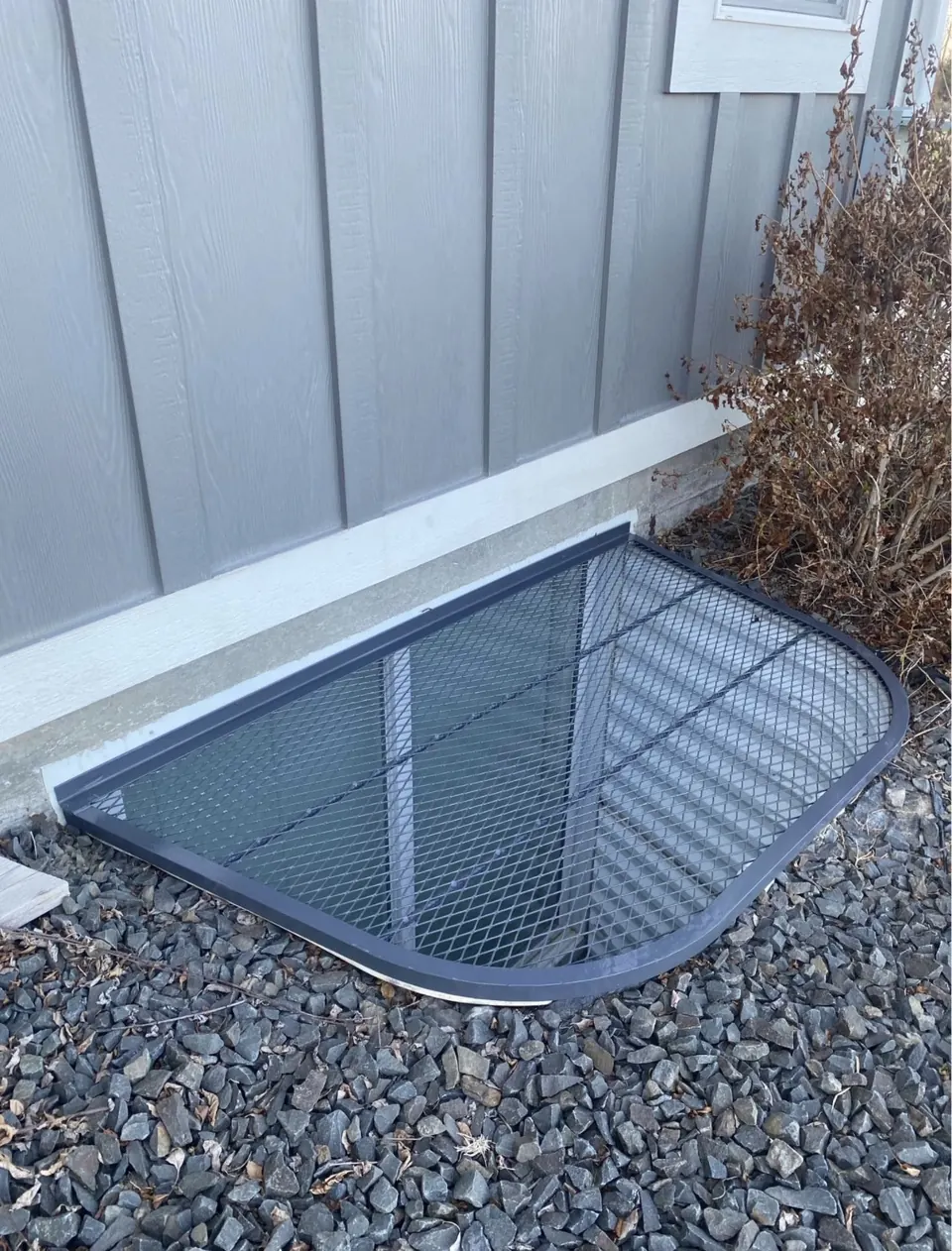 Completed black metal window well cover beside a home